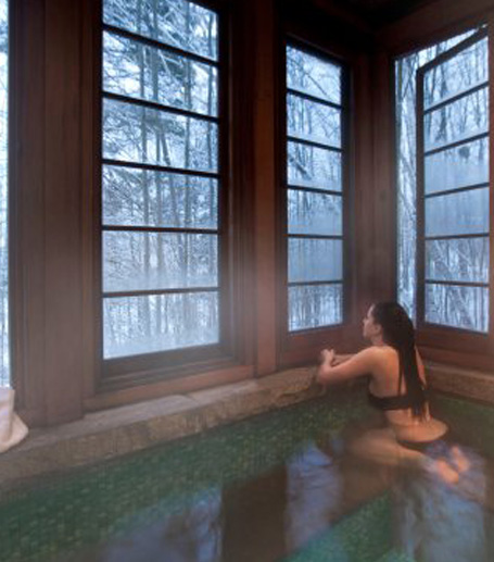 a woman sitting in hot water pool looking at snow outside